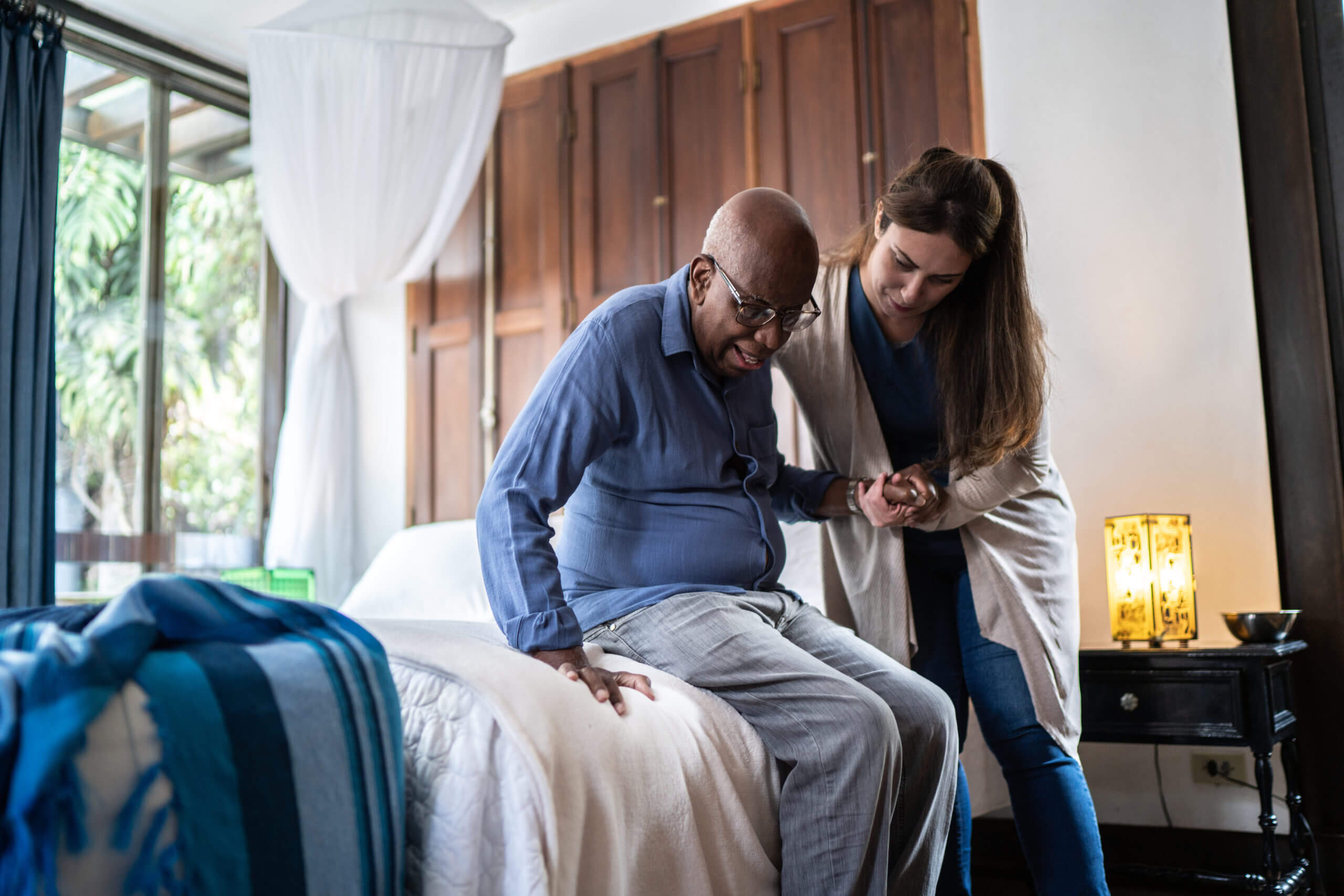 caregiver assisting senior man get out of bed